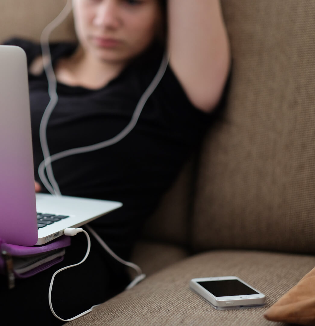 Woman on couch with laptop and earbuds