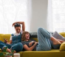 two girls lounge on a yellow couch